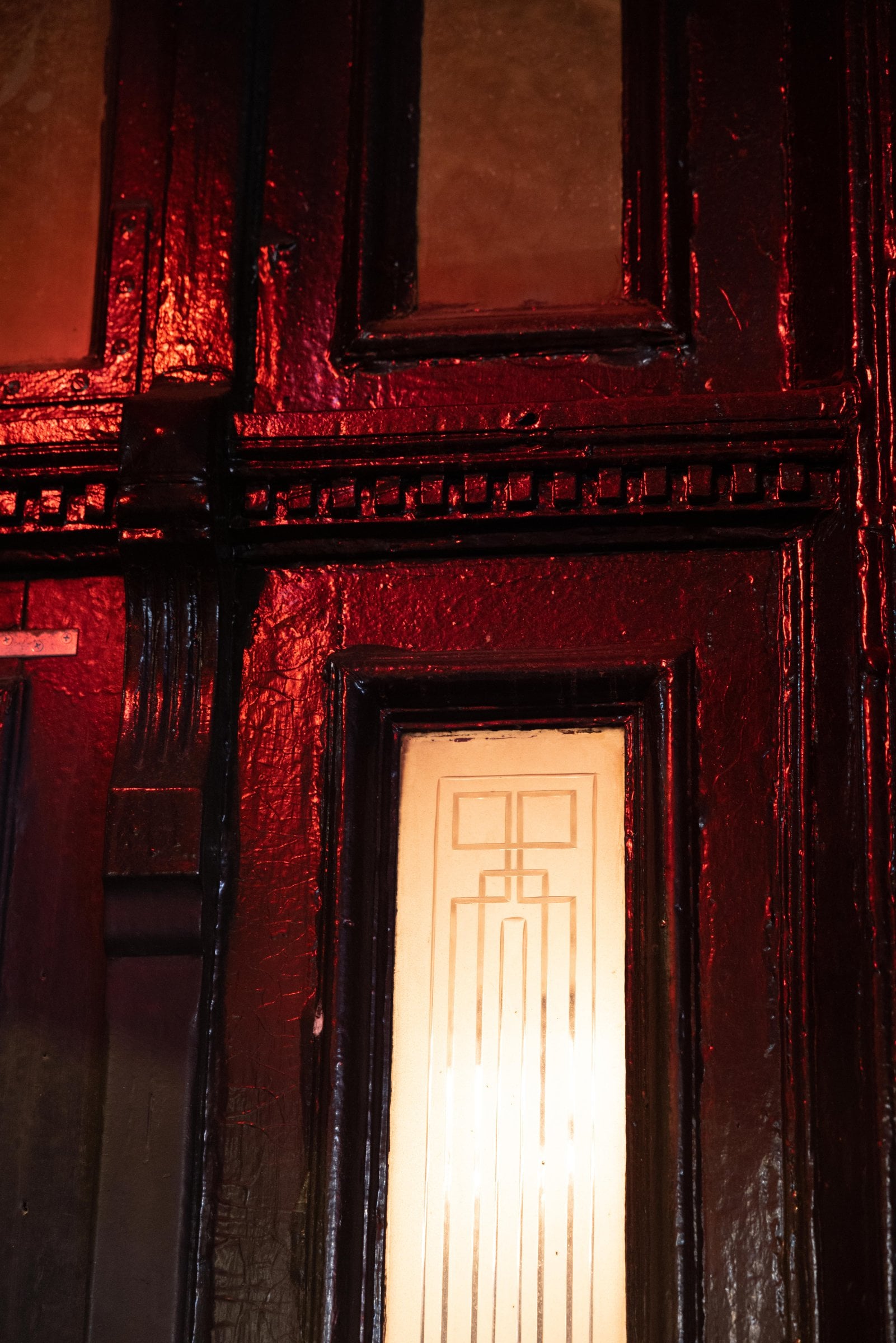 Dark wooden door panels and patterned glass illuminated by red light