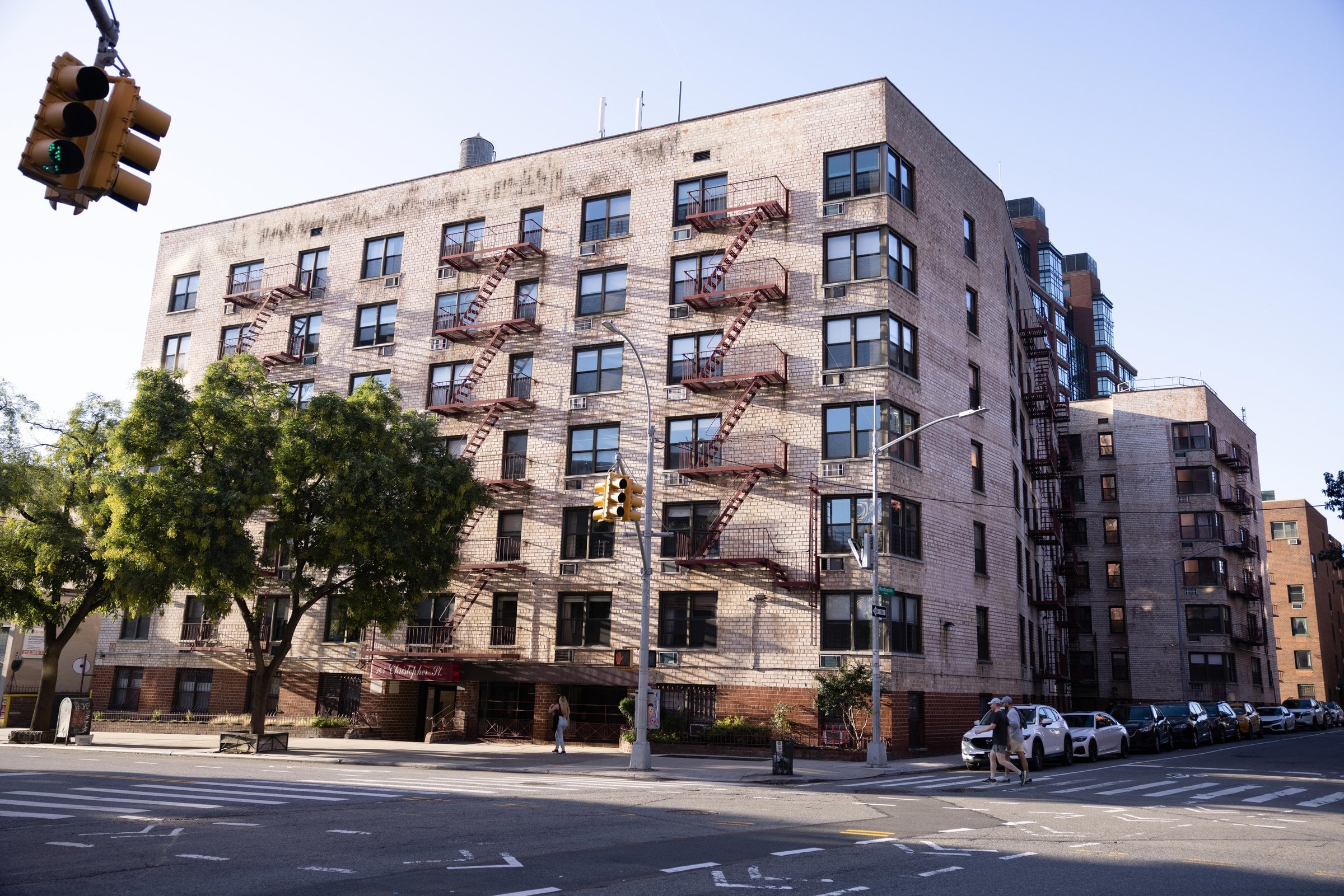 Brick apartment building with fire escapes beside a street intersection