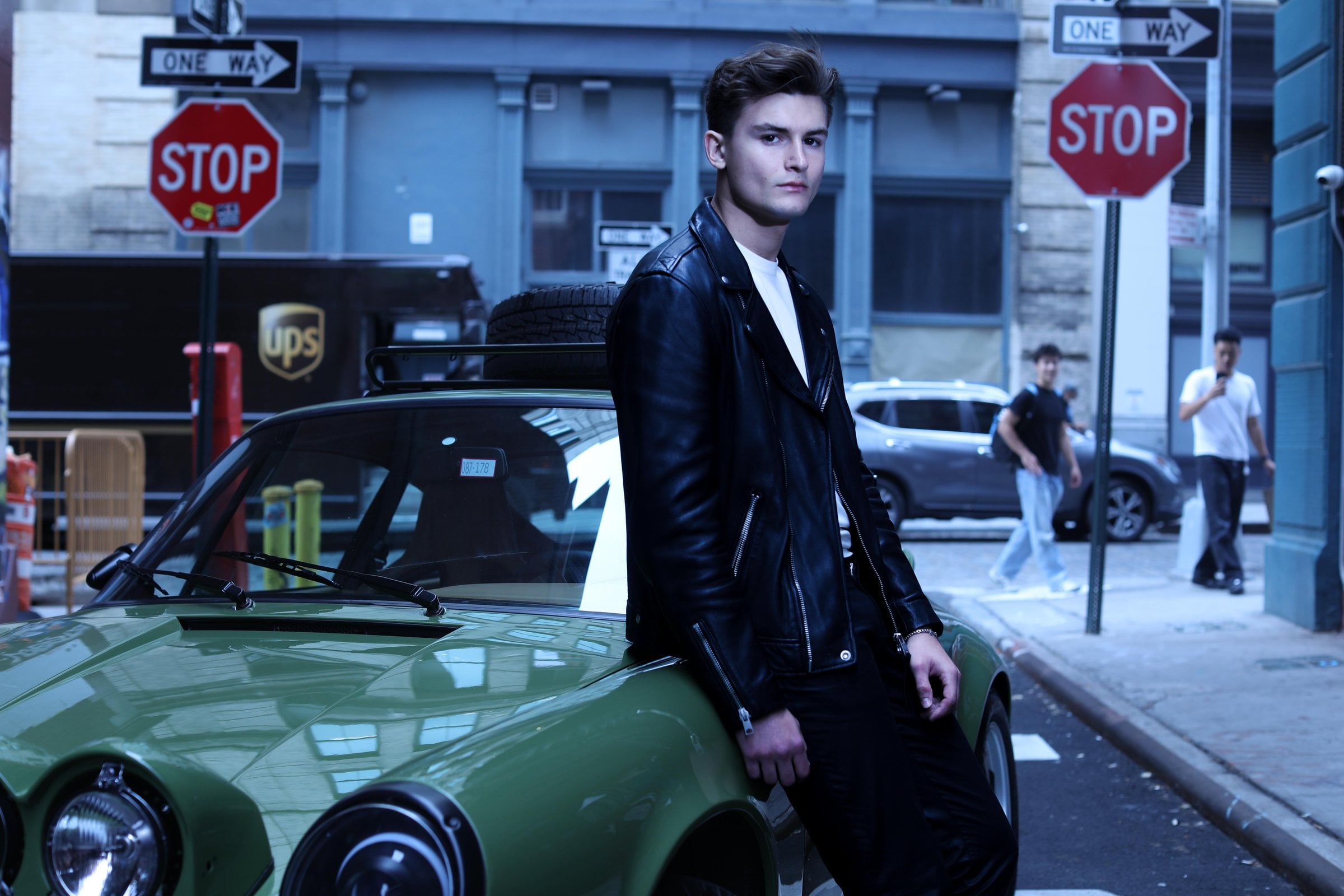 Person in a leather jacket leaning against a green car