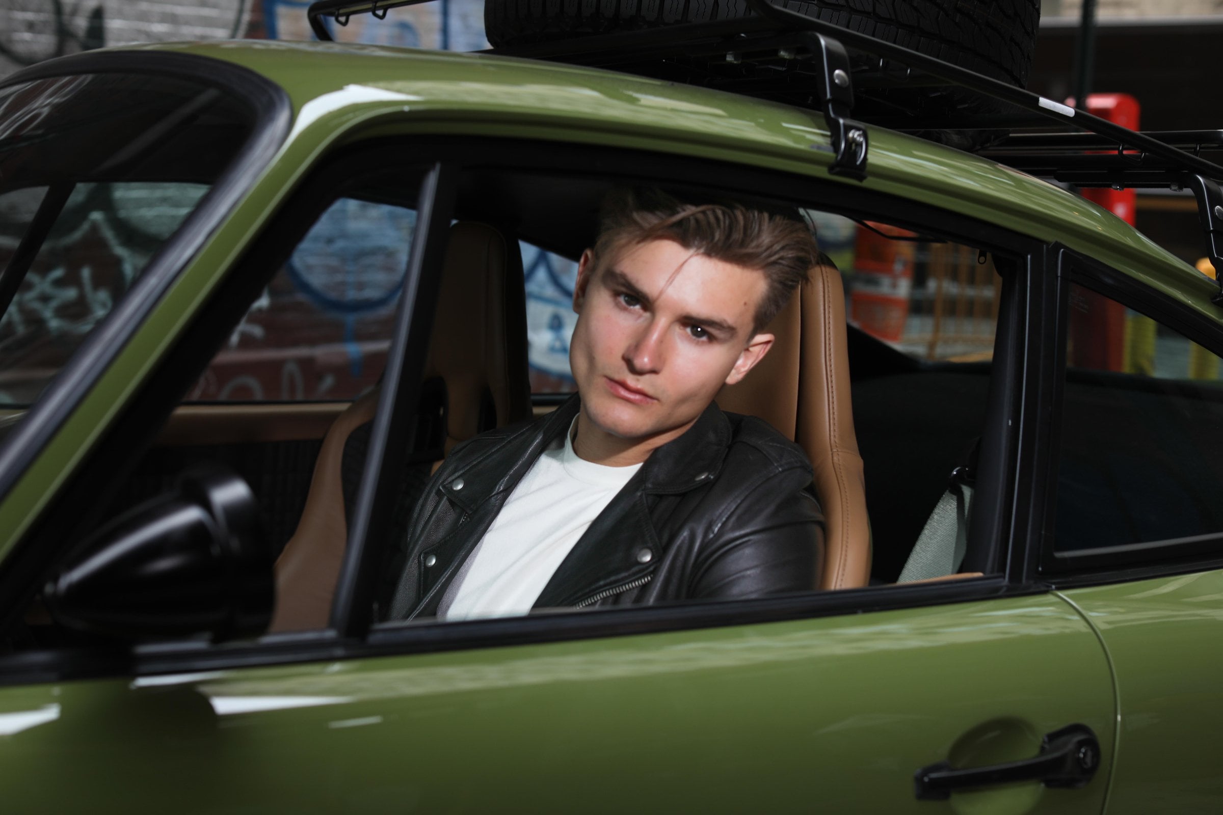 Person in a leather jacket seated inside a green car