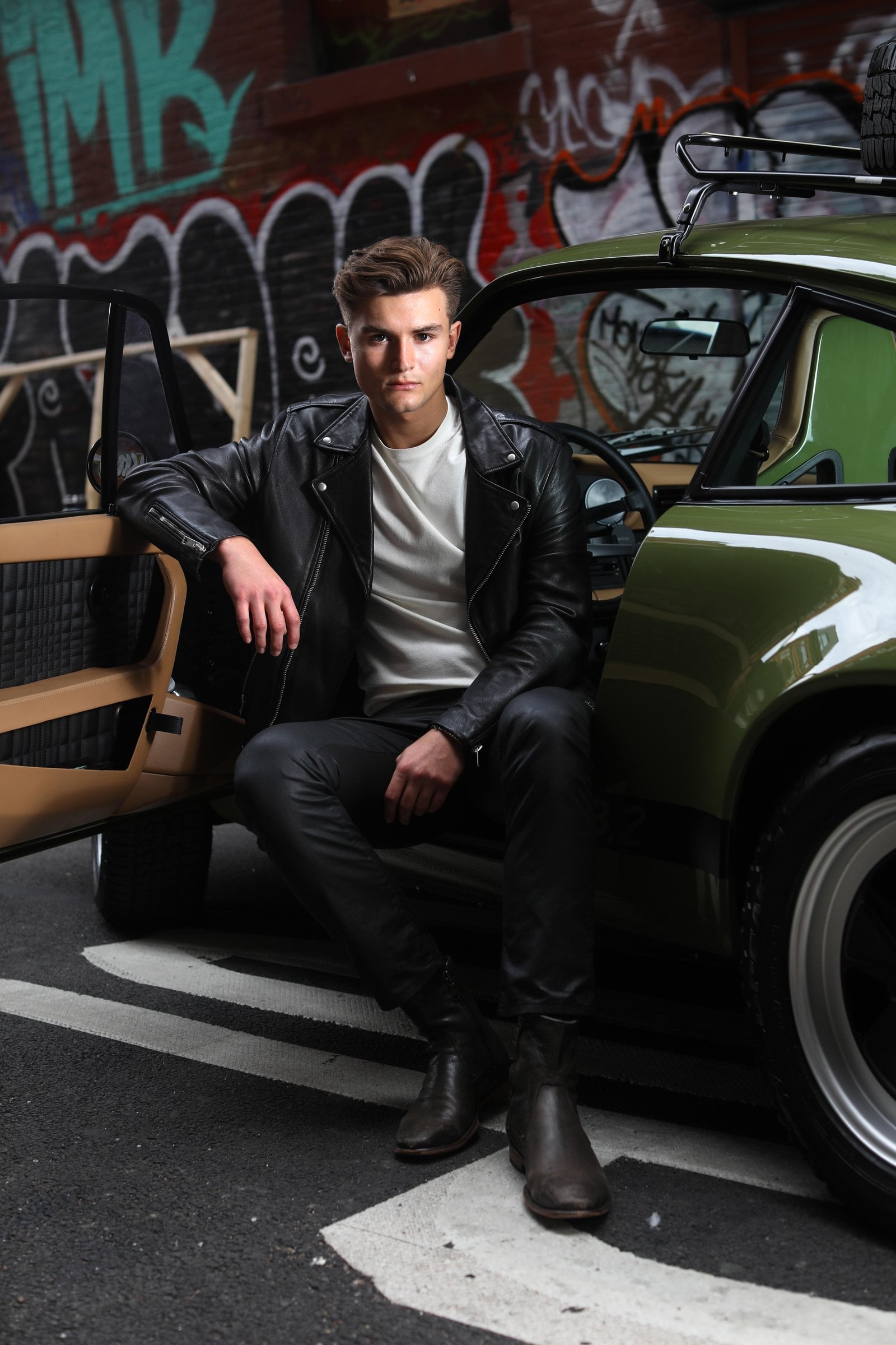 Person sitting in an open car doorway beside a graffiti wall