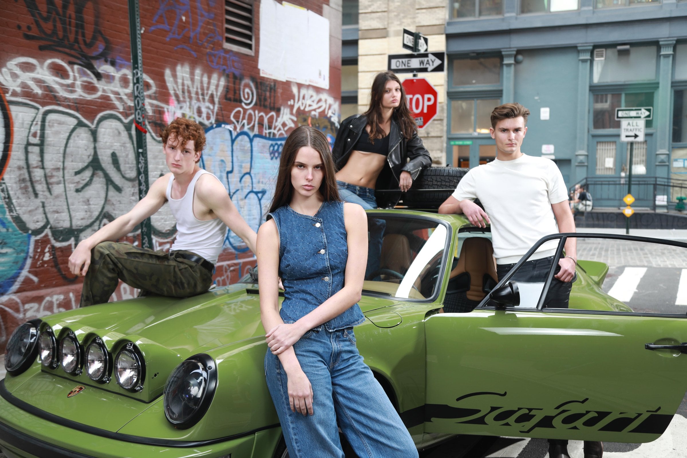 Four people posing beside a green car with its door open