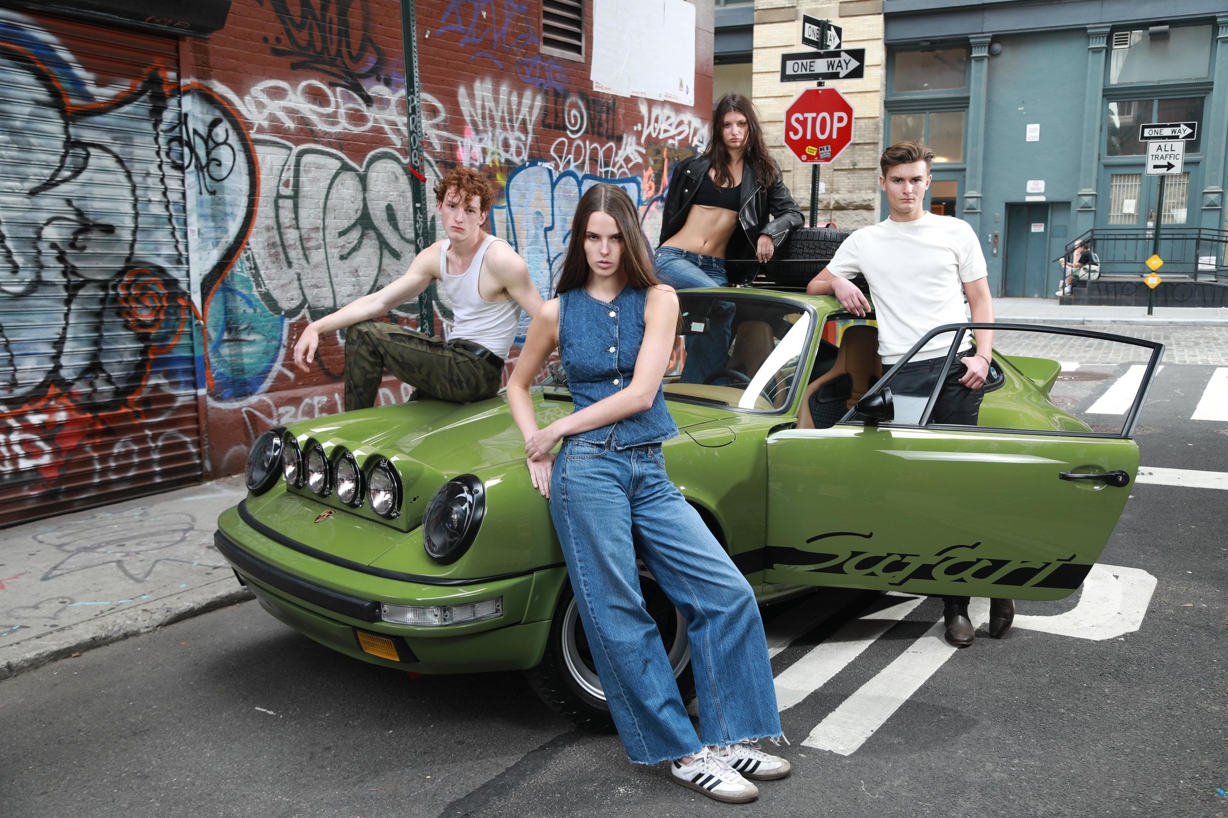 Person in denim standing before three people and a green car