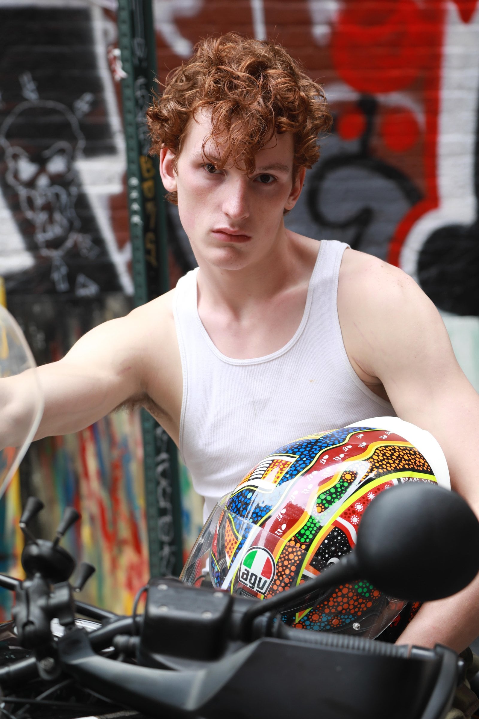 Person with curly hair holding a colorful helmet beside motorcycle handlebars