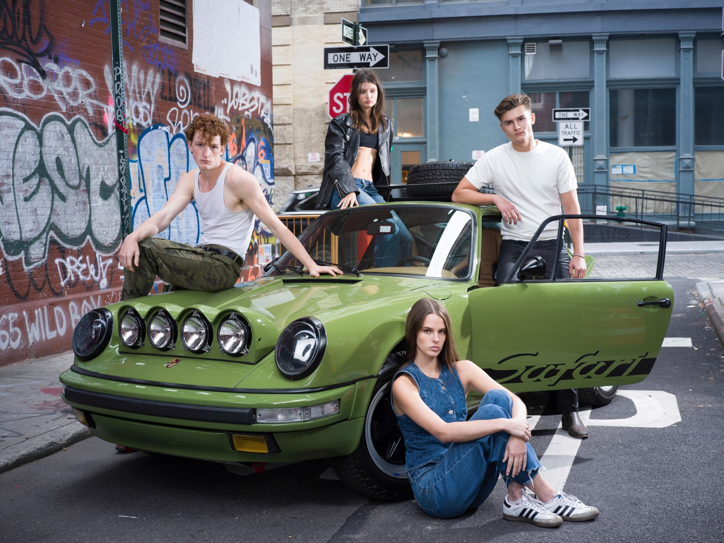 Four people around a green car, one seated beside its wheel