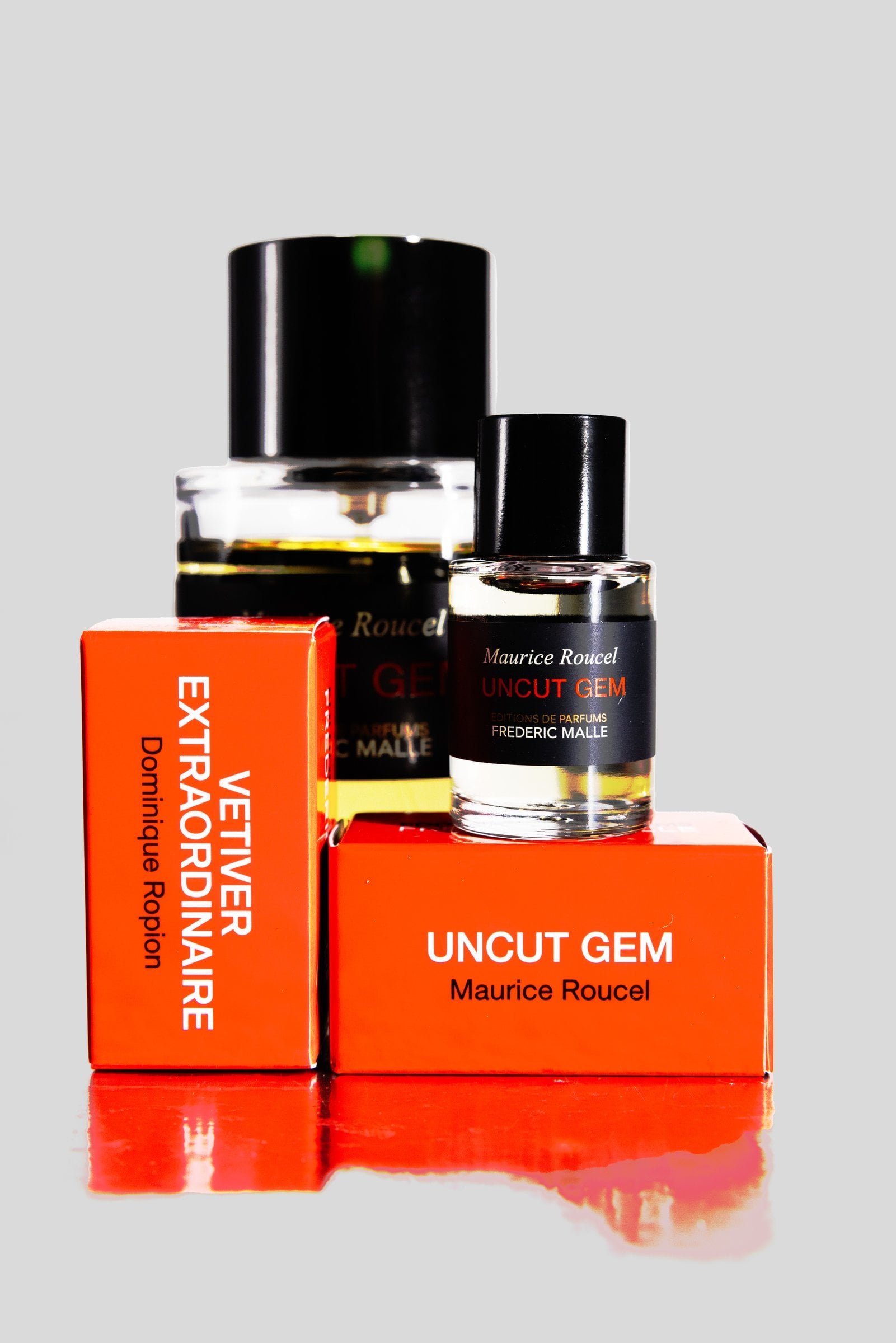 Two perfume bottles and orange boxes on a reflective surface
