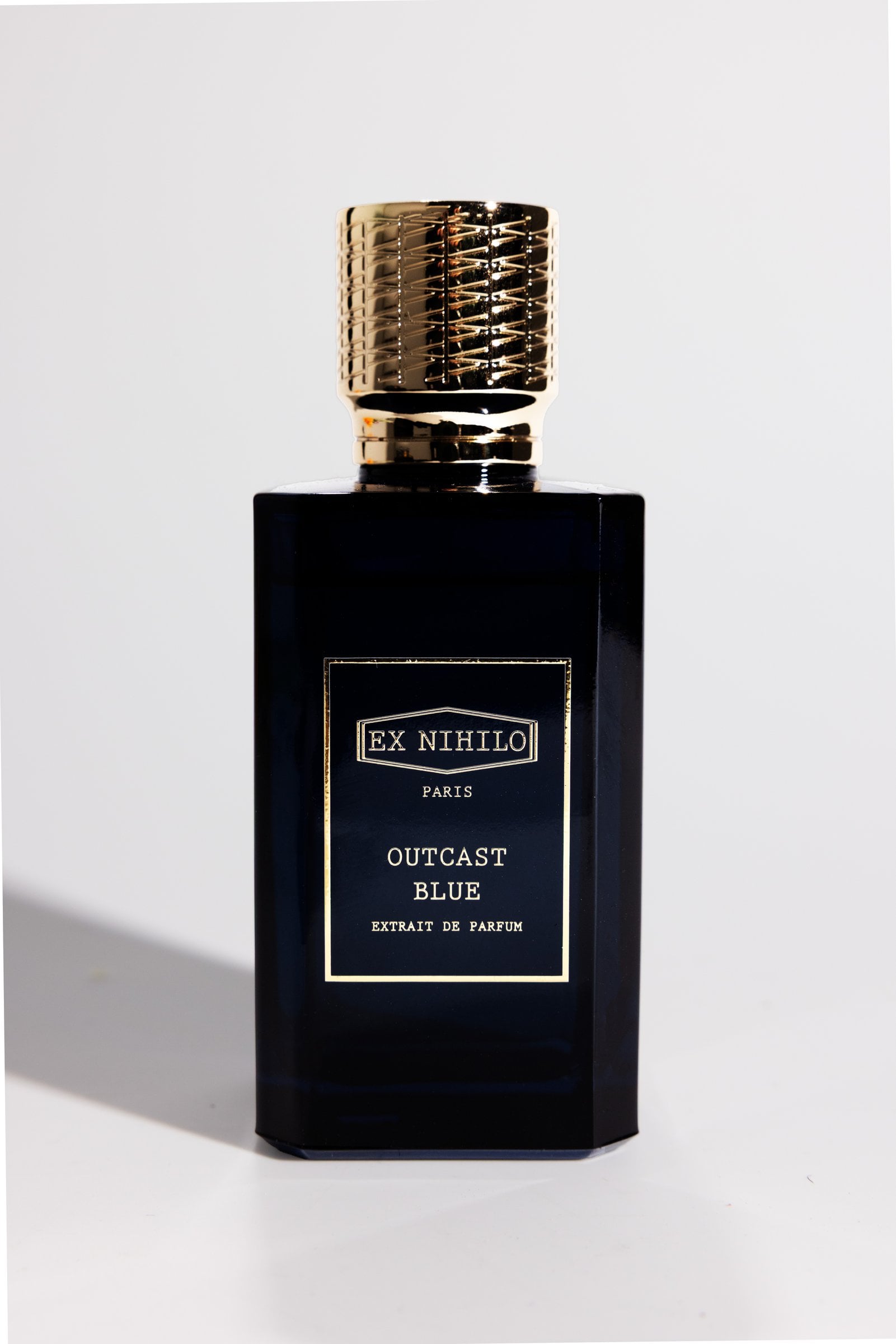 Dark rectangular perfume bottle with a gold cap casting a shadow