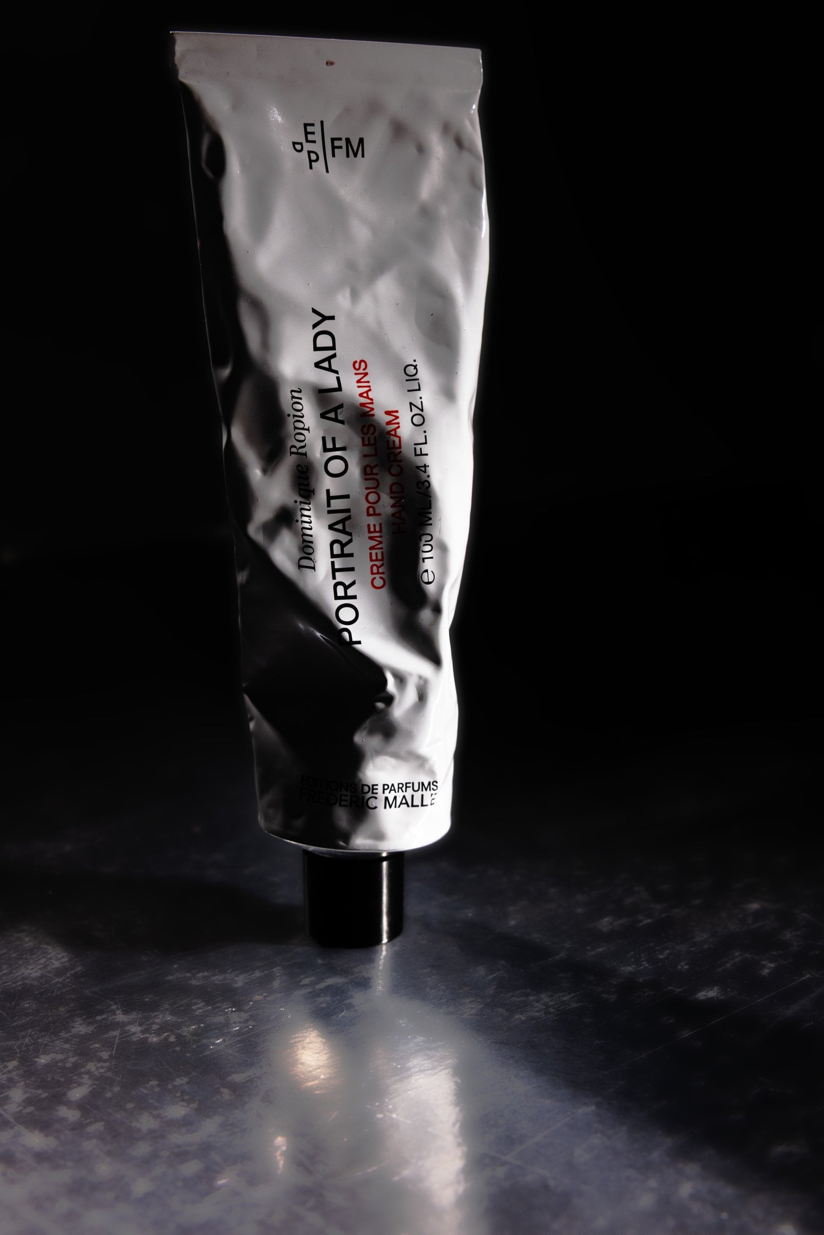 Silver hand cream tube standing on a dark reflective surface