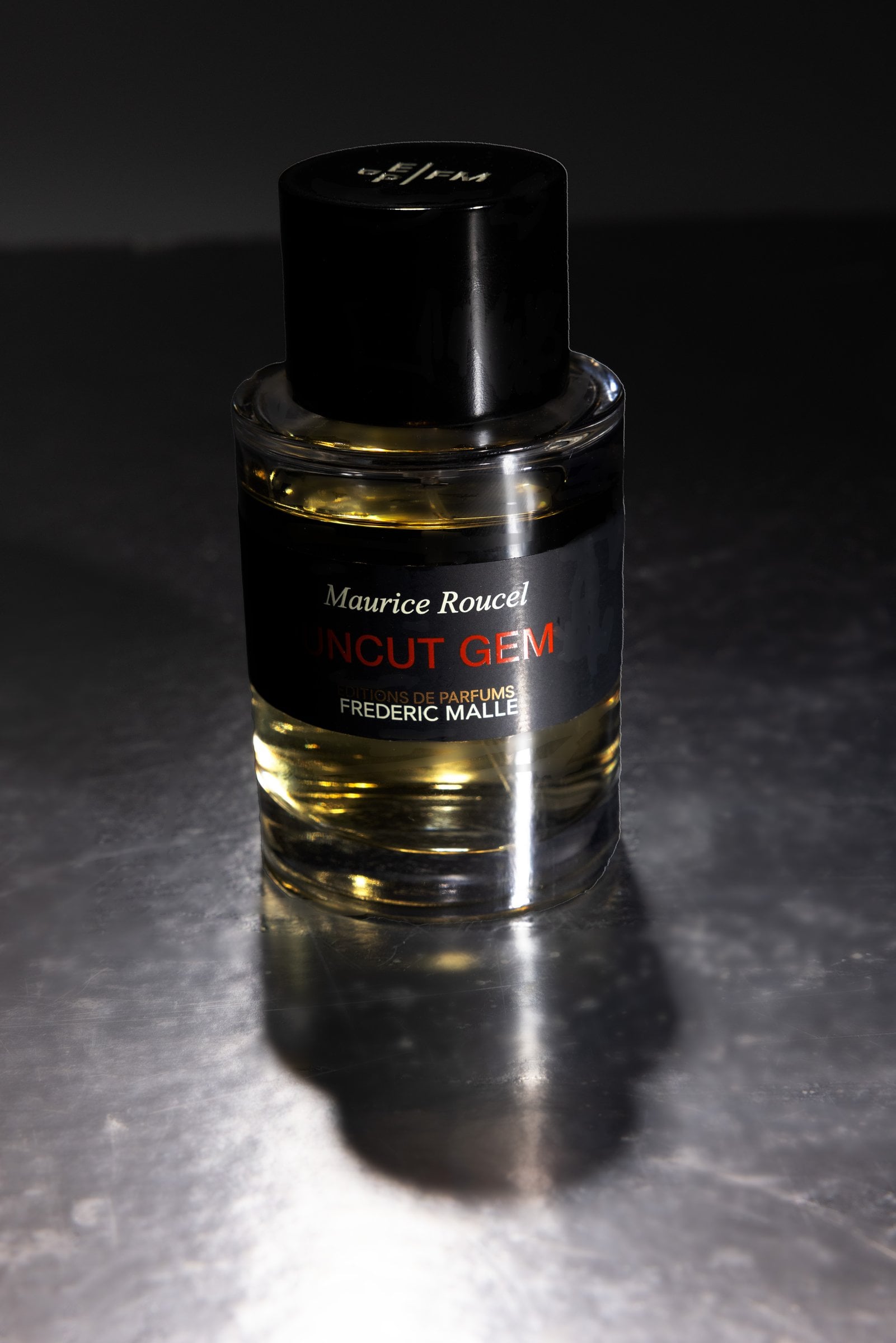 Glass perfume bottle with a black cap on reflective metal